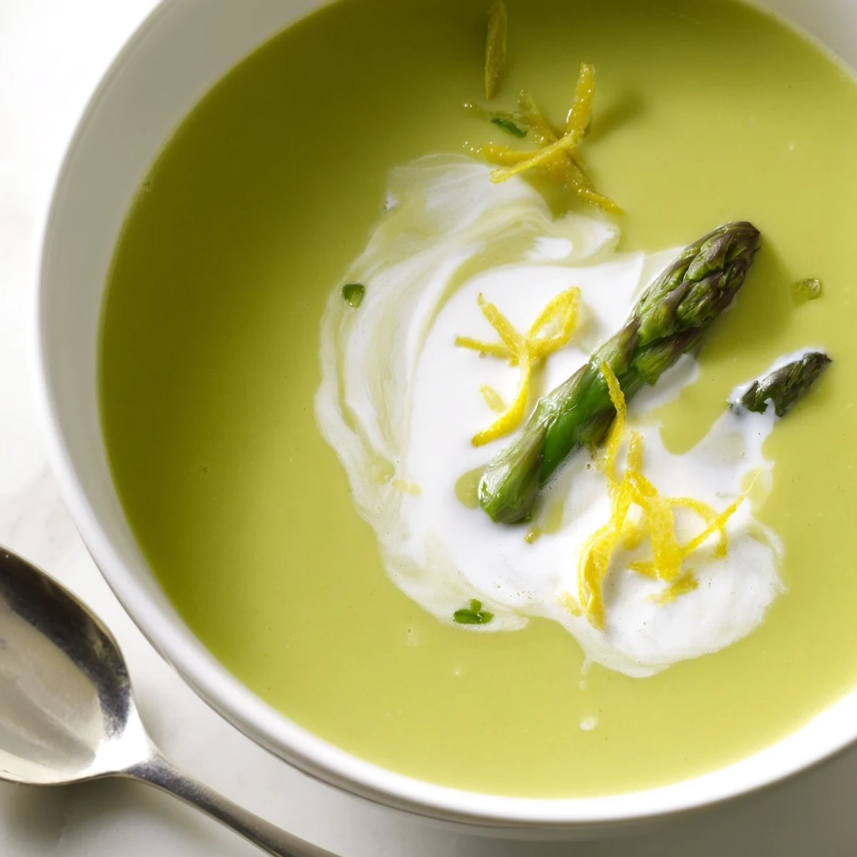 Creamy Asparagus Soup with Lemon and Crème Fraîche in a white bowl, garnished with fresh asparagus tips and chopped chives.