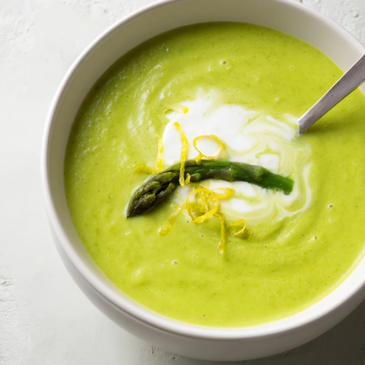 Creamy Asparagus Soup with Lemon and Crème Fraîche in a rustic bowl, showing a smooth green texture and a decorative swirl on top.