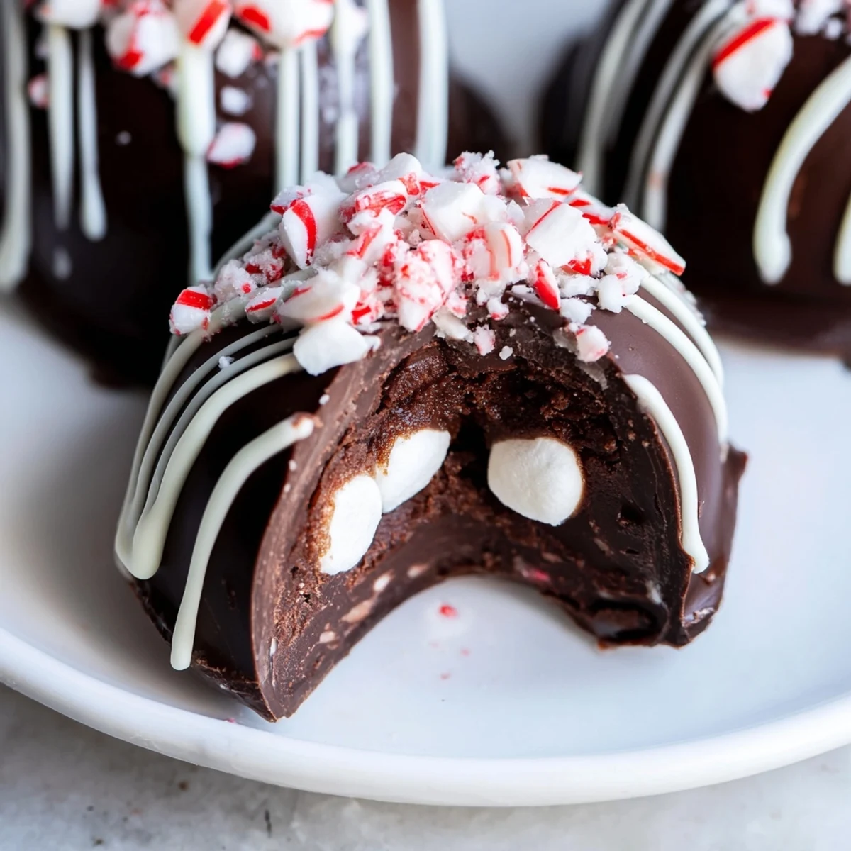 Peppermint Hot Cocoa Bombs with Marshmallows sit on a snowy white board, half-dipped in white chocolate and dusted with crushed candy canes for a festive treat.