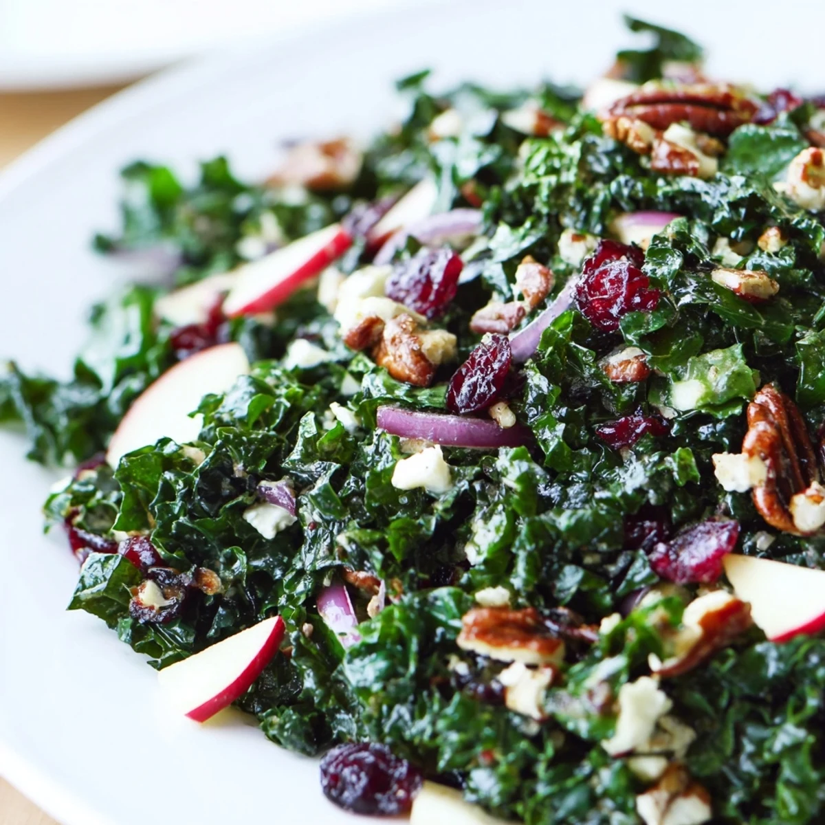 Winter Kale Salad with Cranberries topped with crumbled feta, sliced red onion, and toasted pecans on a rustic wood table.