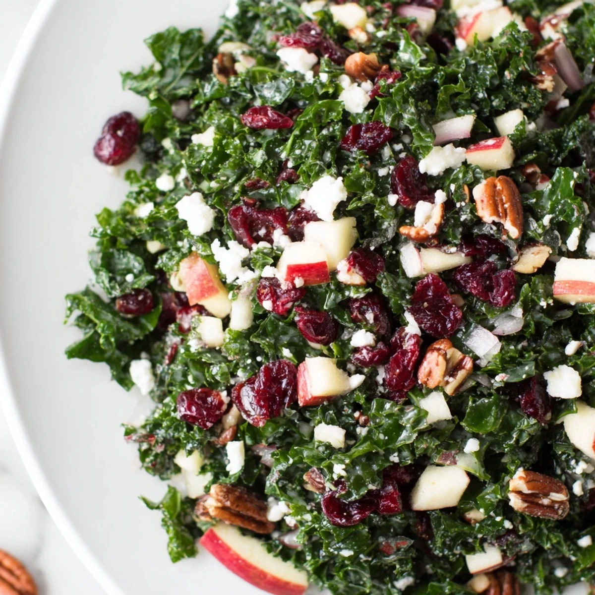 A fresh Winter Kale Salad with Cranberries paired with diced apple and a zesty citrus vinaigrette in a white bowl.