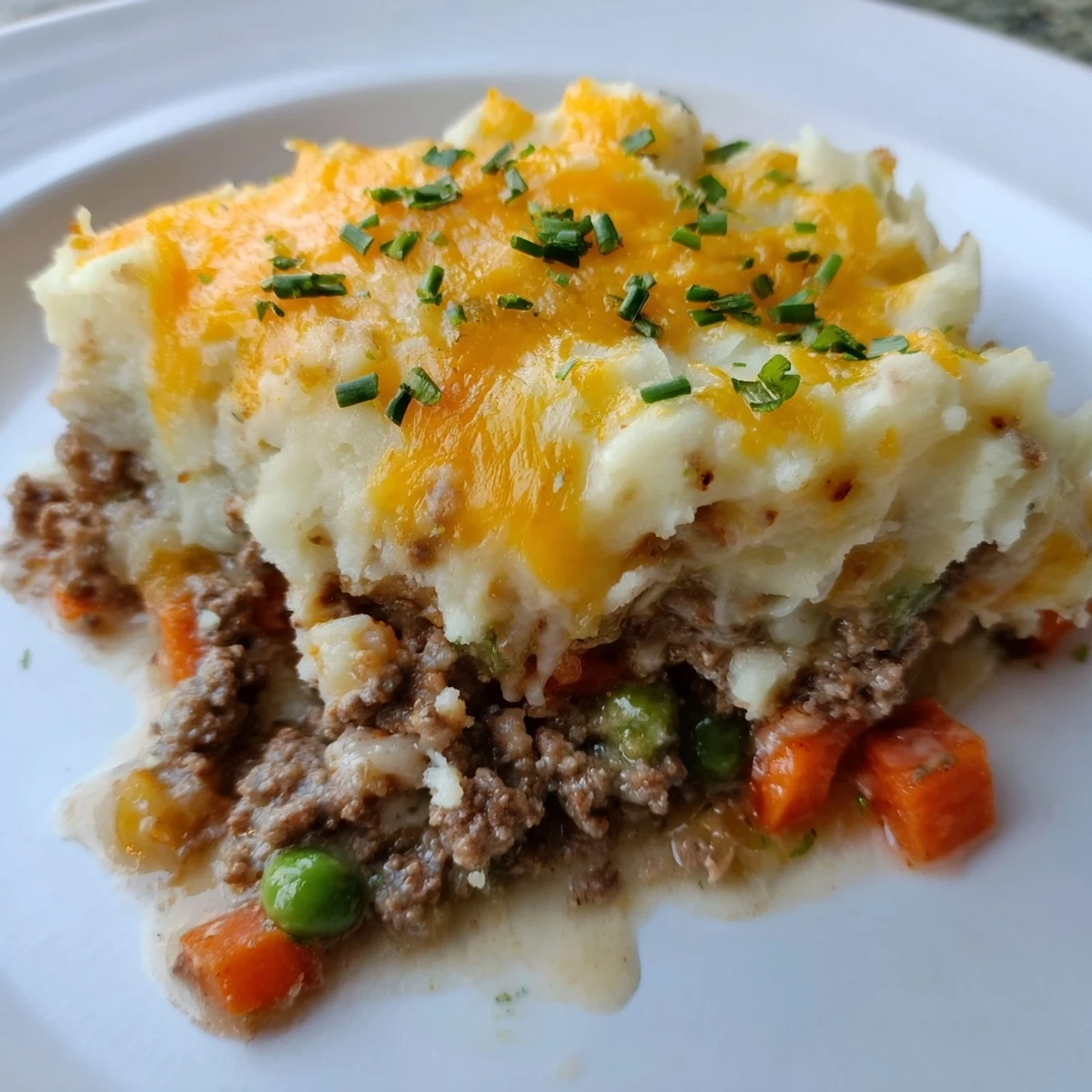 Serving suggestion of Beef Shepherds Pie scoop revealing savory ground beef, peas, and carrots beneath creamy cheesy potatoes.
