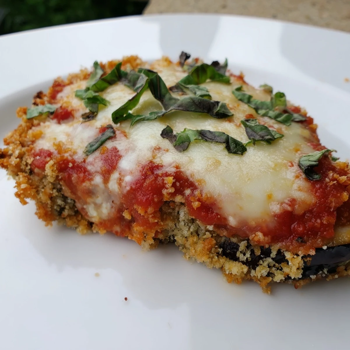 Golden-brown baked eggplant slices layered with rich marinara sauce and melted mozzarella in a ceramic dish.
