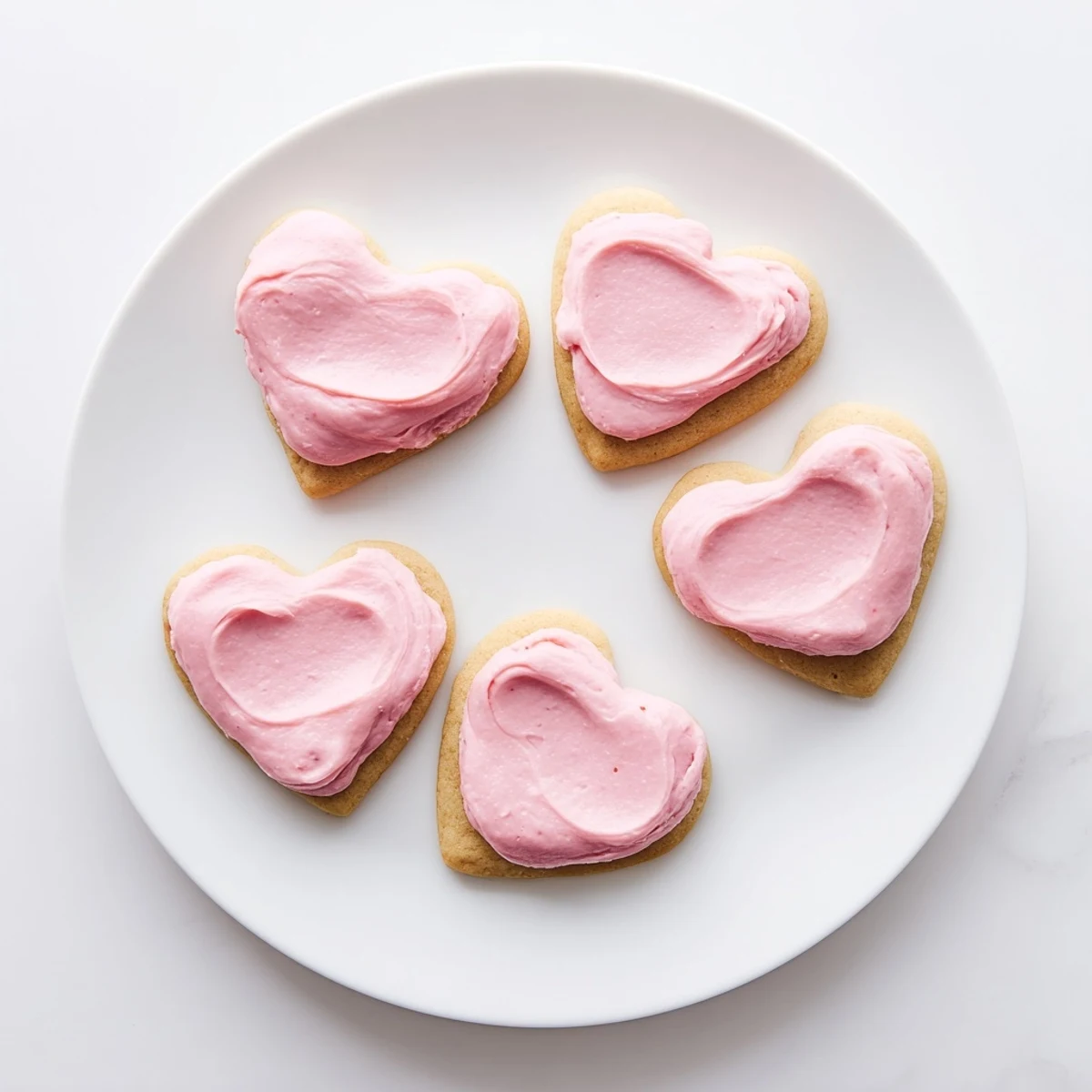 Heart Cookies with pink frosting arranged on a white plate, ready to serve with a glass of milk.  