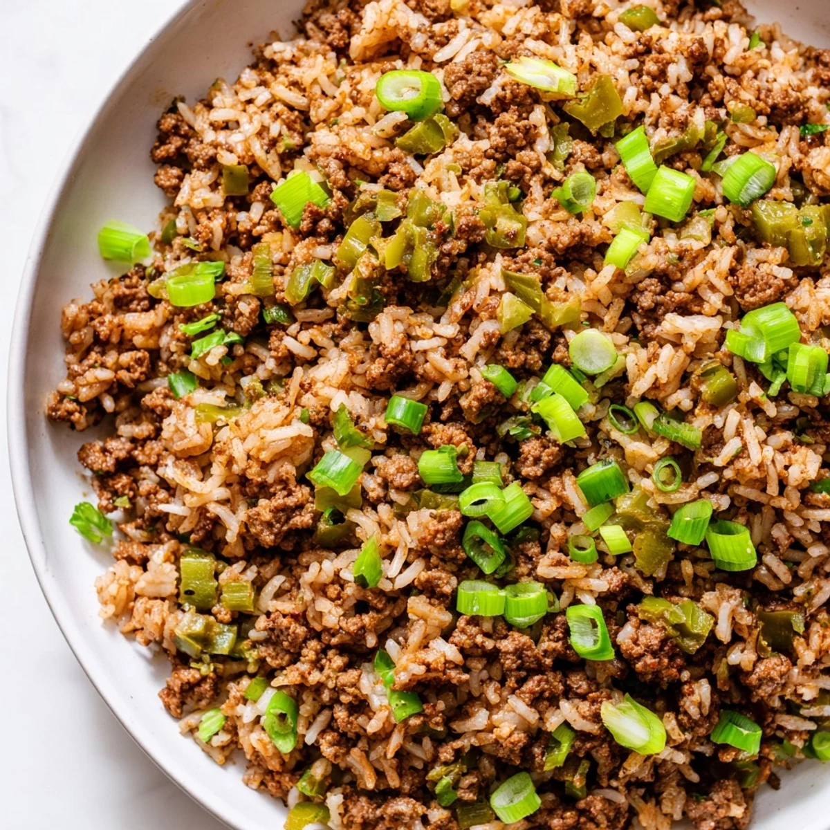 Savory Mardi Gras Dirty Rice with Beef plated beside hot sauce and a crisp green salad.