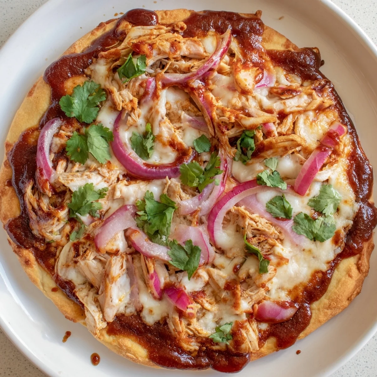The finished BBQ Chicken Pizza rests on a wooden board, showcasing melted mozzarella and smoked Gouda bubbling over tender chicken chunks and crimson red onion slices, garnished with fresh cilantro.