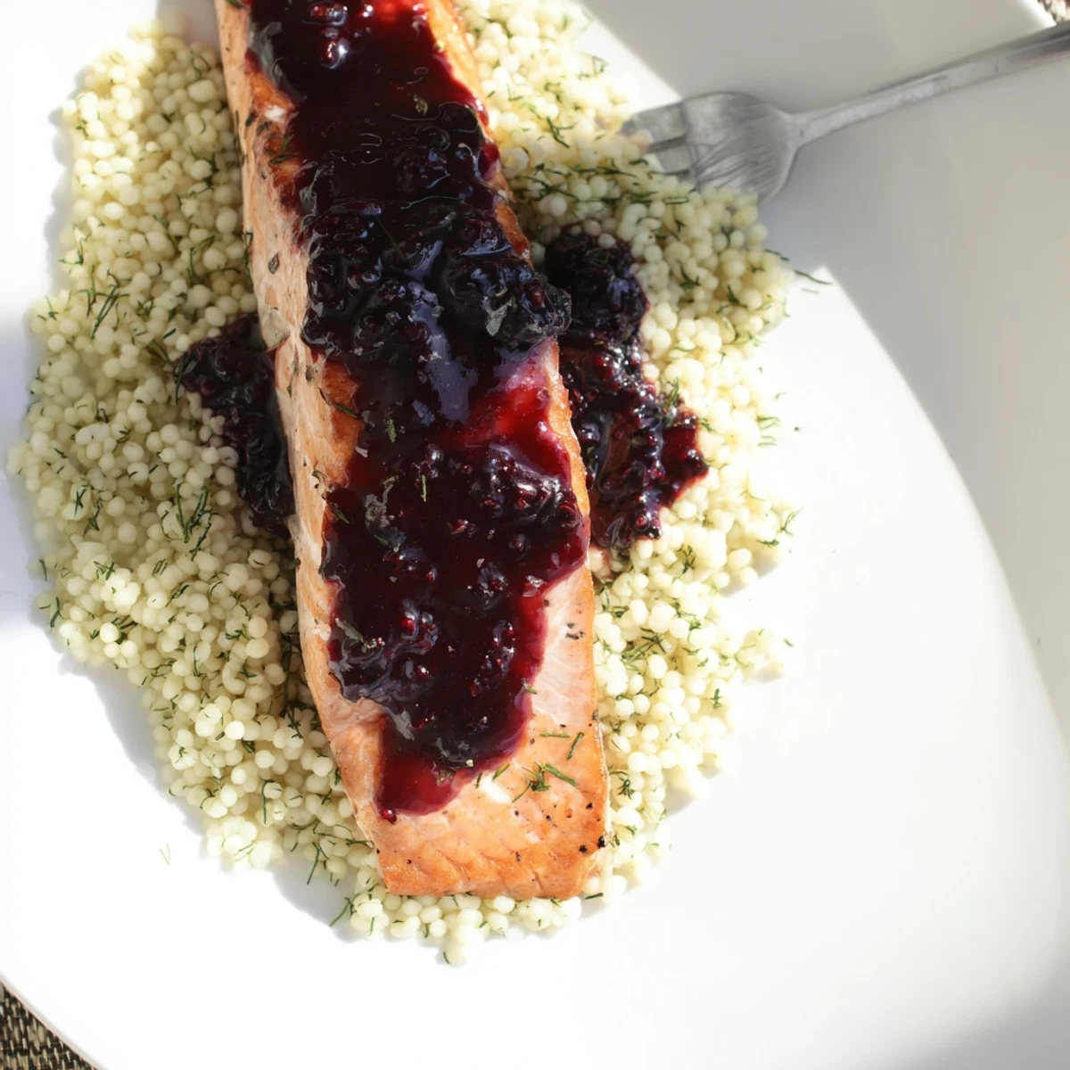 Tender blueberry glazed salmon paired with aromatic lemon couscous and fresh parsley on a rustic white plate.