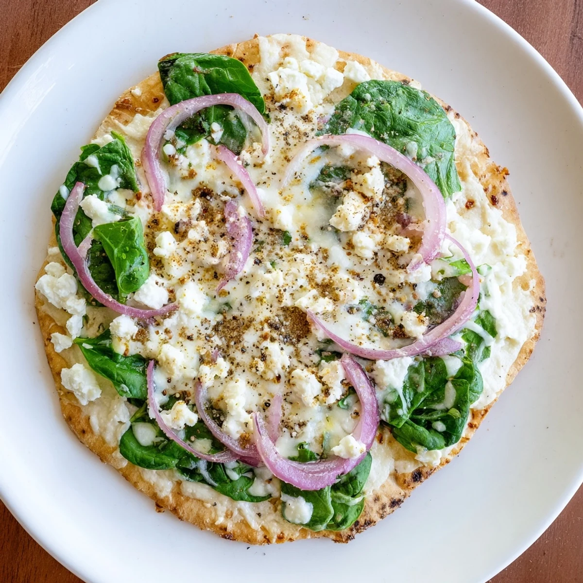 A close-up of a freshly baked Spinach and Feta Flatbread Pizza on a wooden board, featuring melted mozzarella, bright green spinach, and crumbled feta cheese.