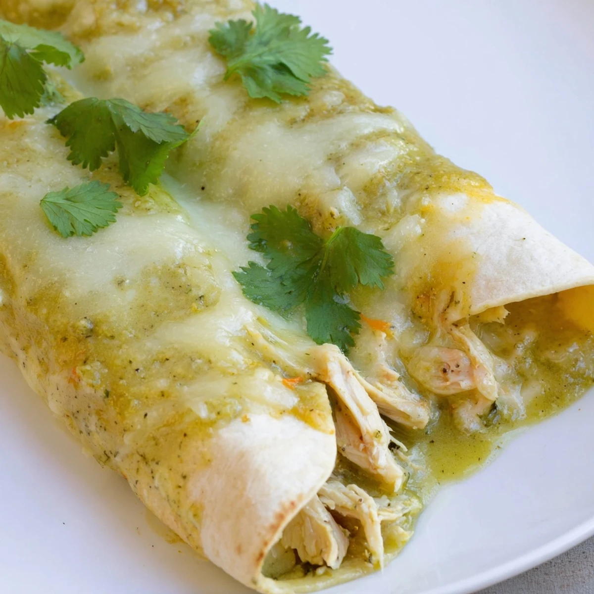 Golden-brown Green Enchiladas With Chicken are baked in a dish, topped with melted Monterey Jack cheese and fresh cilantro.
