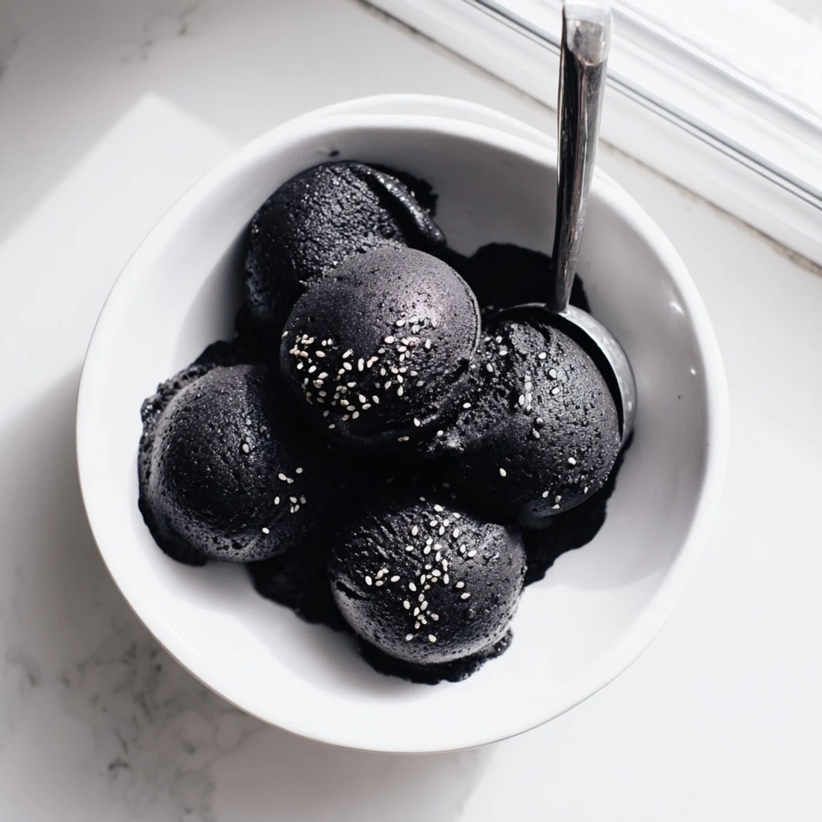 Toasted Black Sesame Ice Cream is shown in a rustic ceramic dish topped with toasted sesame seeds.