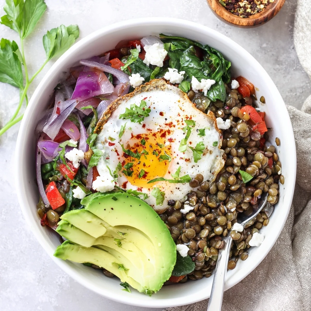 A vibrant Savory Lentil Breakfast Bowl topped with a runny egg yolk, fresh herbs, and sliced avocado for a nourishing start.