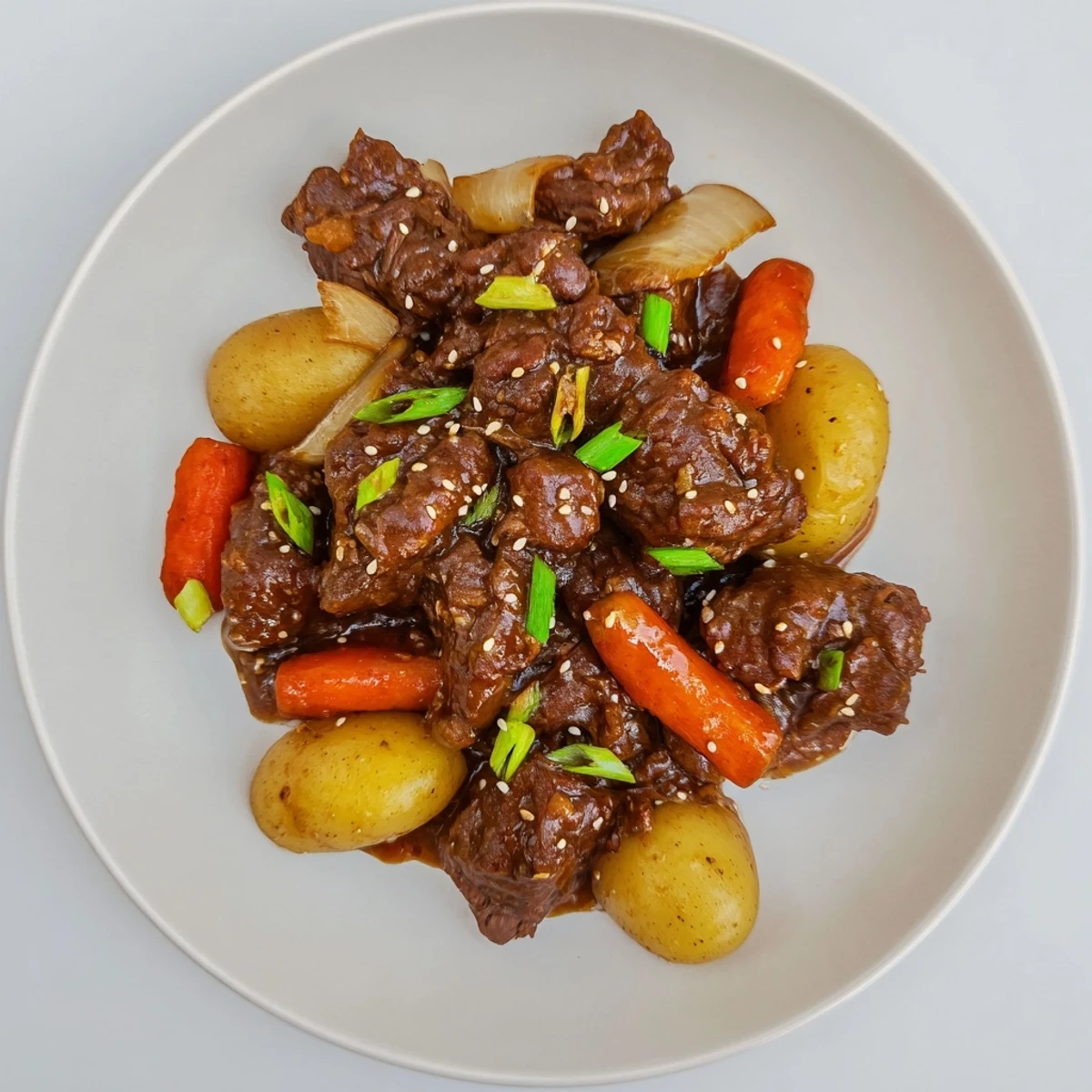 Fork-tender Slow Cooker Korean Beef Pot Roast served with glazed carrots, baby potatoes, and scallions for a hearty meal.