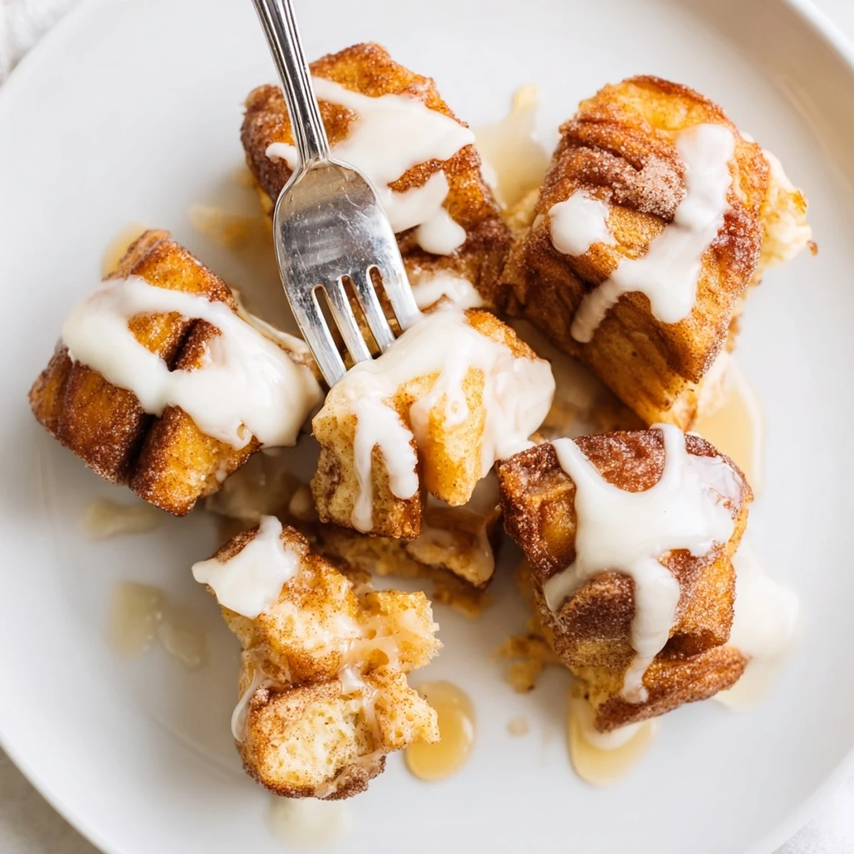 Warm Cinnamon Roll French Toast Bites drizzled with icing and fresh berries on a plate.