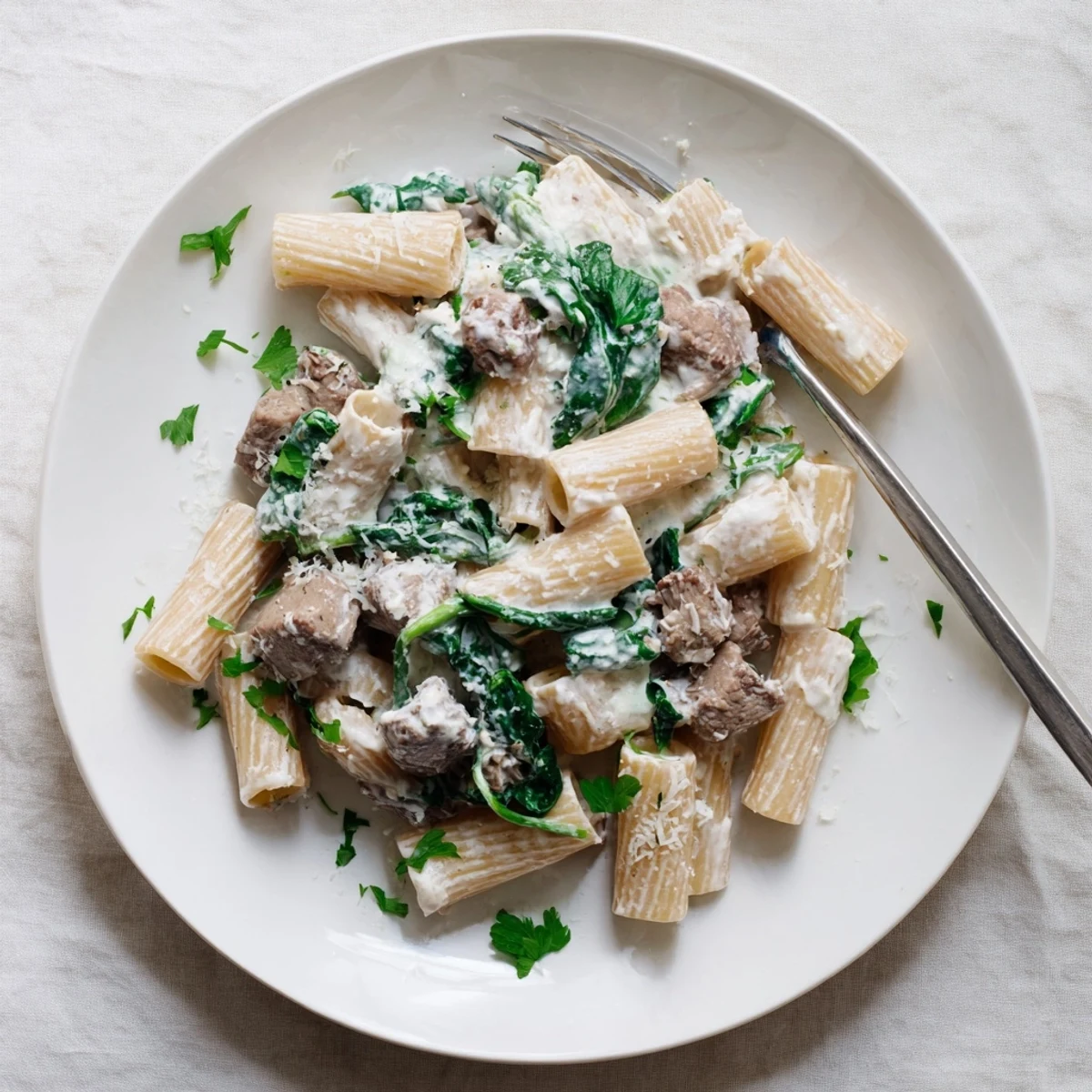 Creamy high protein beef pasta tossed in a rich white sauce with tender sliced beef and wilted spinach garnished with fresh parsley.