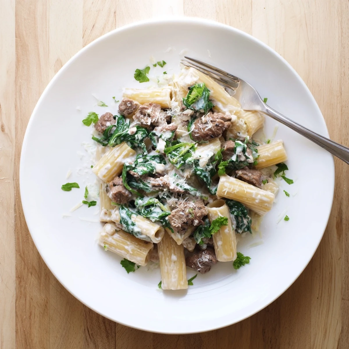 Close up of creamy high protein beef pasta showing al dente noodles mixed with Greek yogurt sauce and browned steak slices topped with Parmesan.
