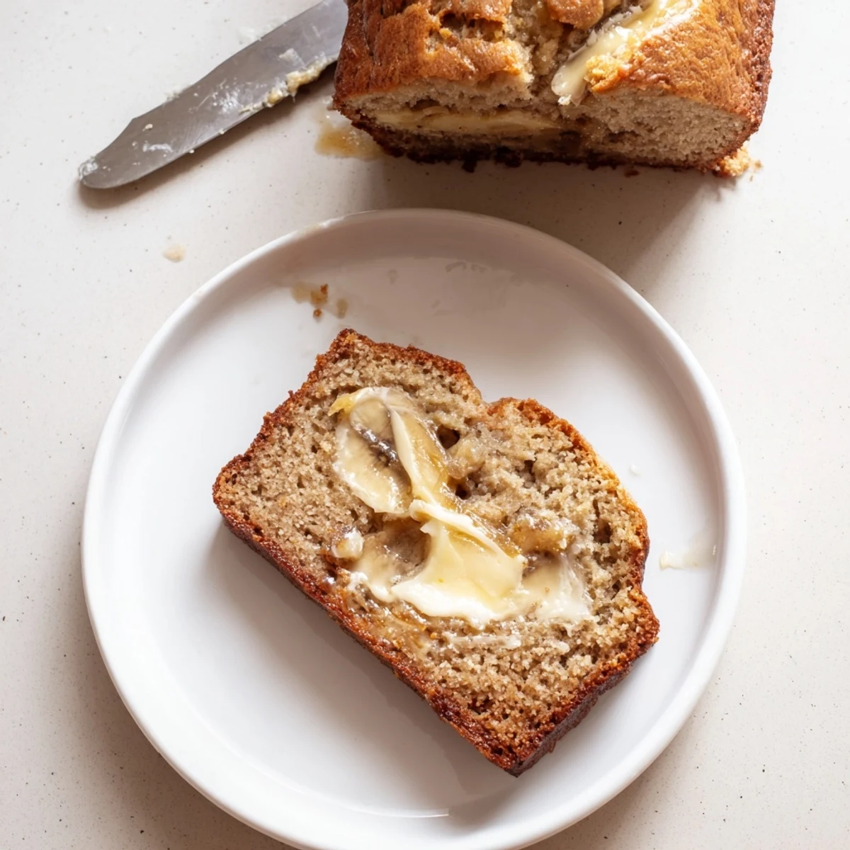 Golden brown moist banana bread loaf with a perfectly crumbly slice on a wooden cutting board