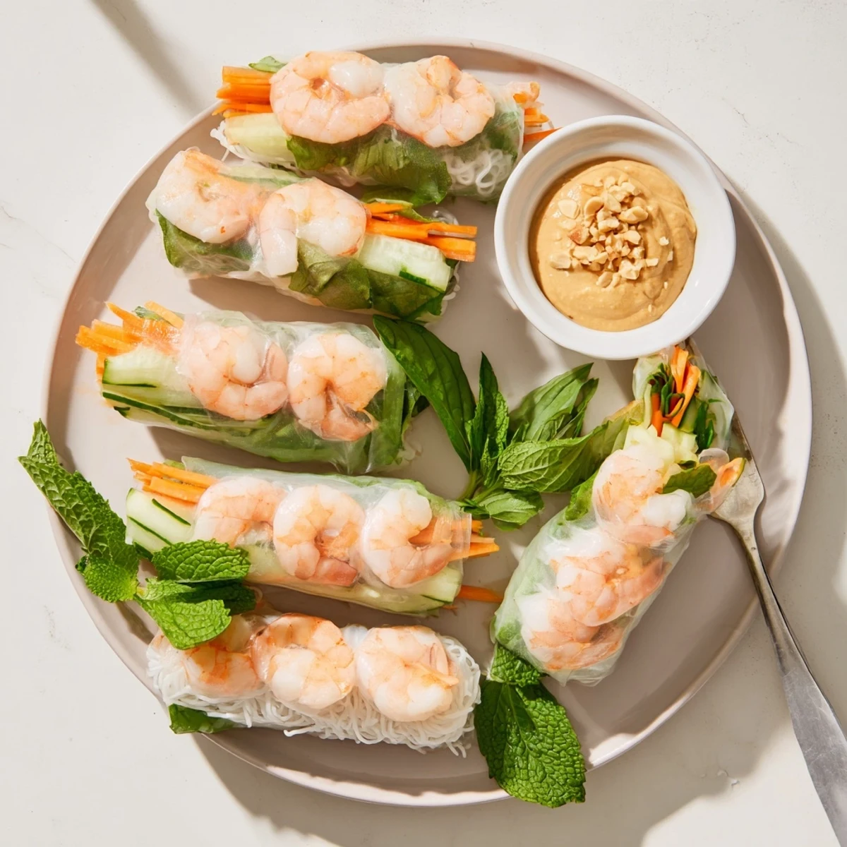 Homemade Vietnamese spring rolls featuring julienned carrots, cucumber, and mint leaves served alongside dark peanut sauce