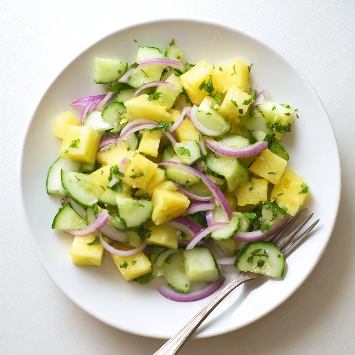 Vibrant pineapple cucumber salad bowl with fresh cilantro and lime drizzle on white background