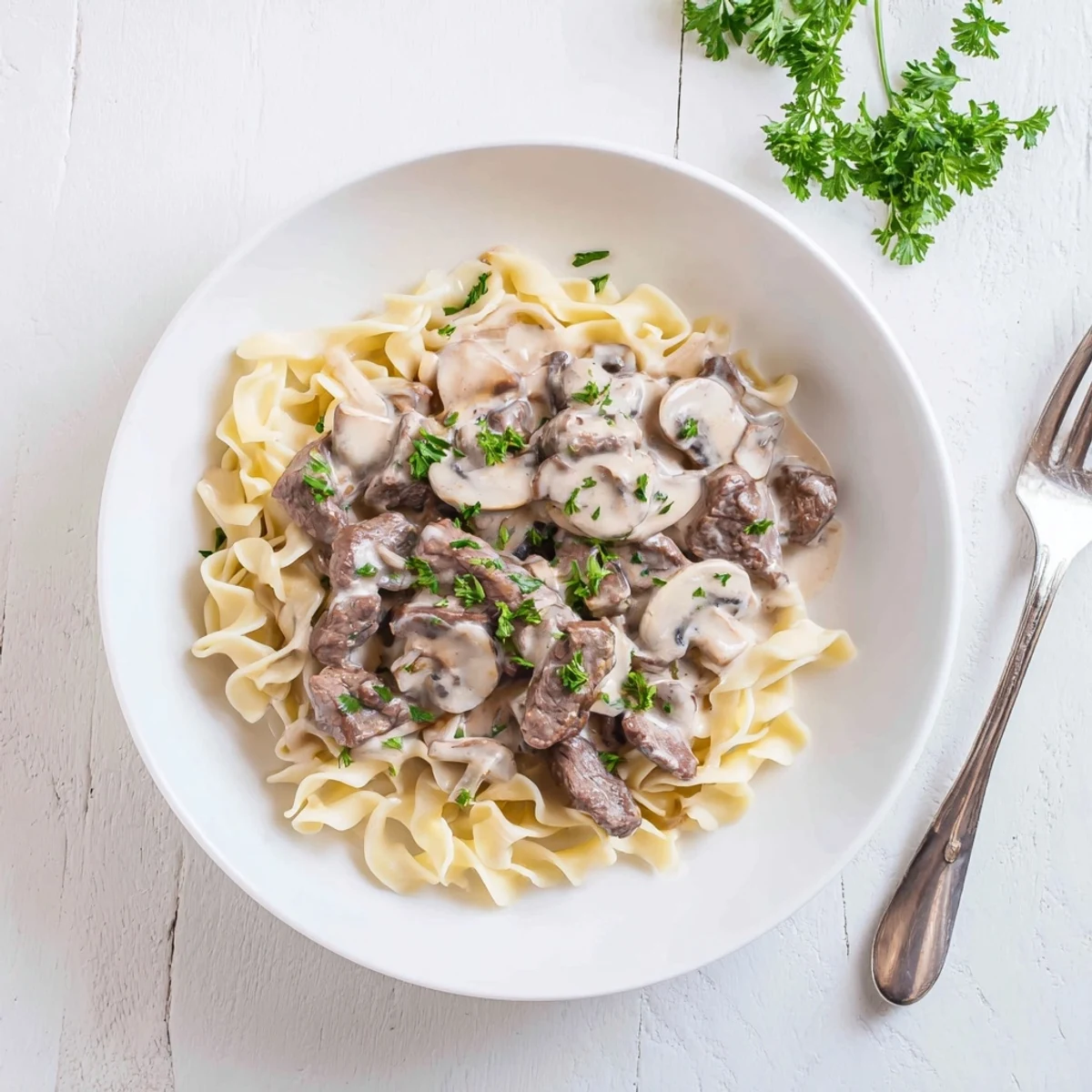 Homemade beef stroganoff plated with fresh parsley garnish over a bed of noodles