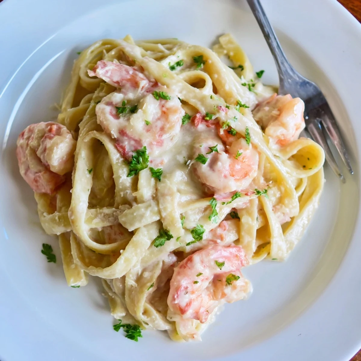 Golden shrimp fettuccine pasta draped in velvety homemade Alfredo sauce with fresh parsley garnish