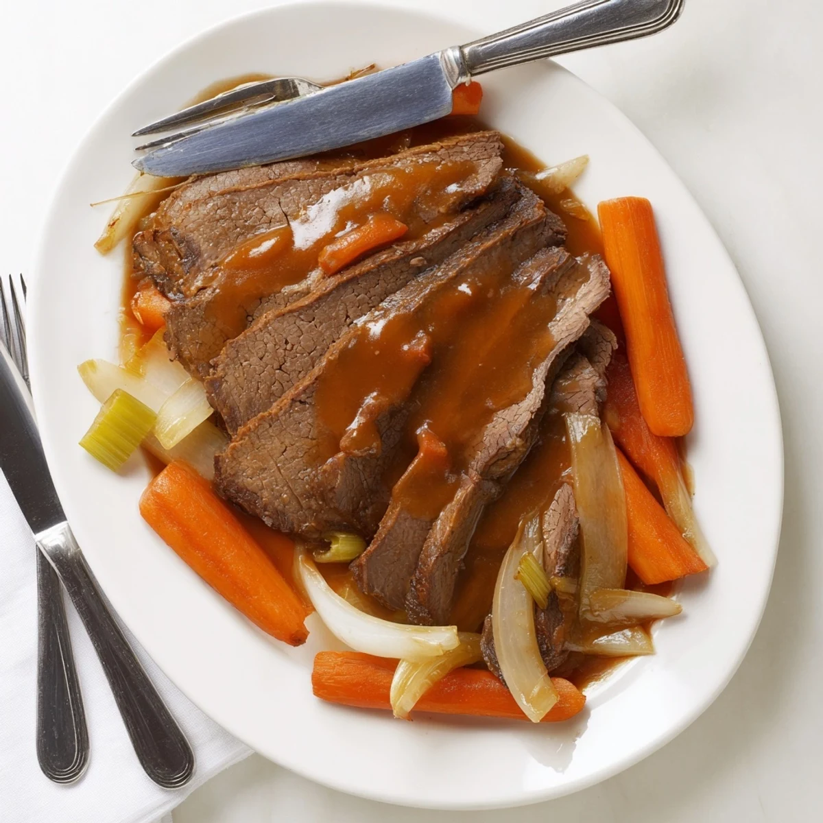 Slices of tender slow cooker beef brisket drizzled with rich dark sauce alongside roasted carrots and onions
