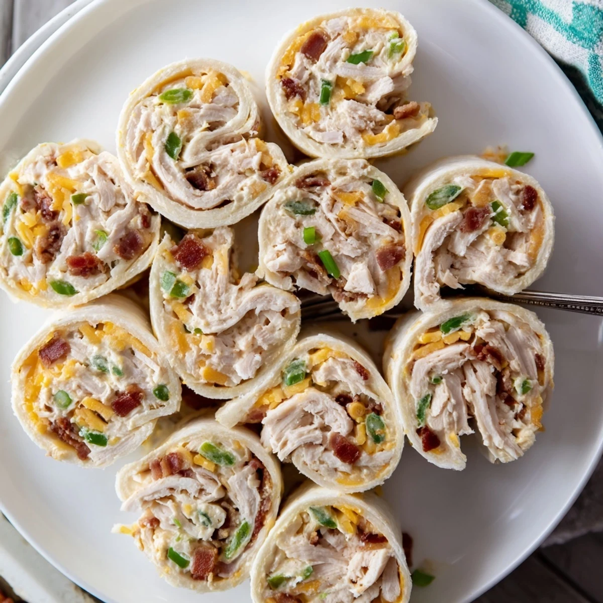 Golden swirls of creamy crack chicken pinwheels topped with bacon and cheddar on a white serving platter