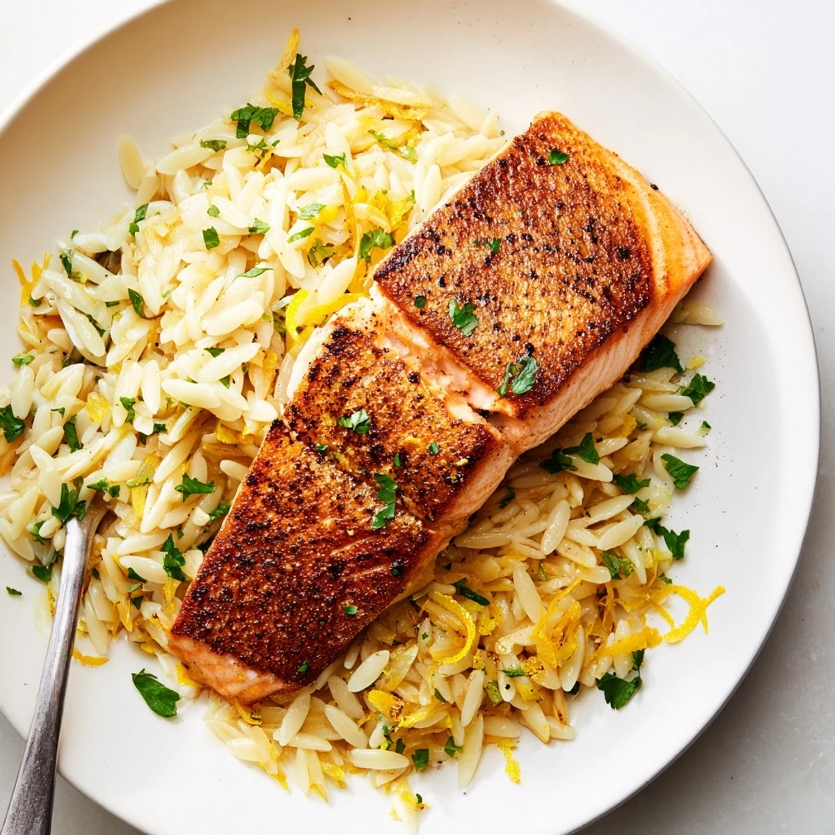 Golden seared salmon fillets resting atop creamy lemon orzo with fresh parsley garnish