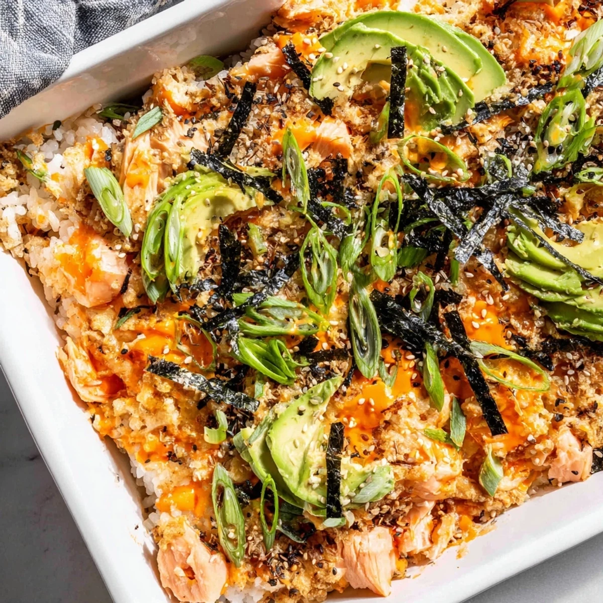 Warm deconstructed salmon sushi bake with furikake seasoning, nori strips, and toasted sesame seeds
