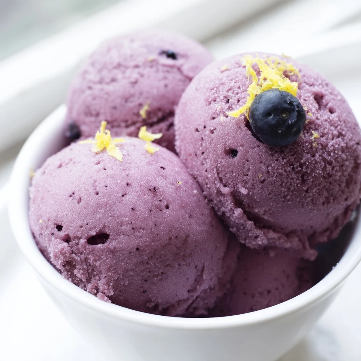 Purple no churn blueberry lemon sorbet scooped into a chilled glass bowl with fresh mint garnish