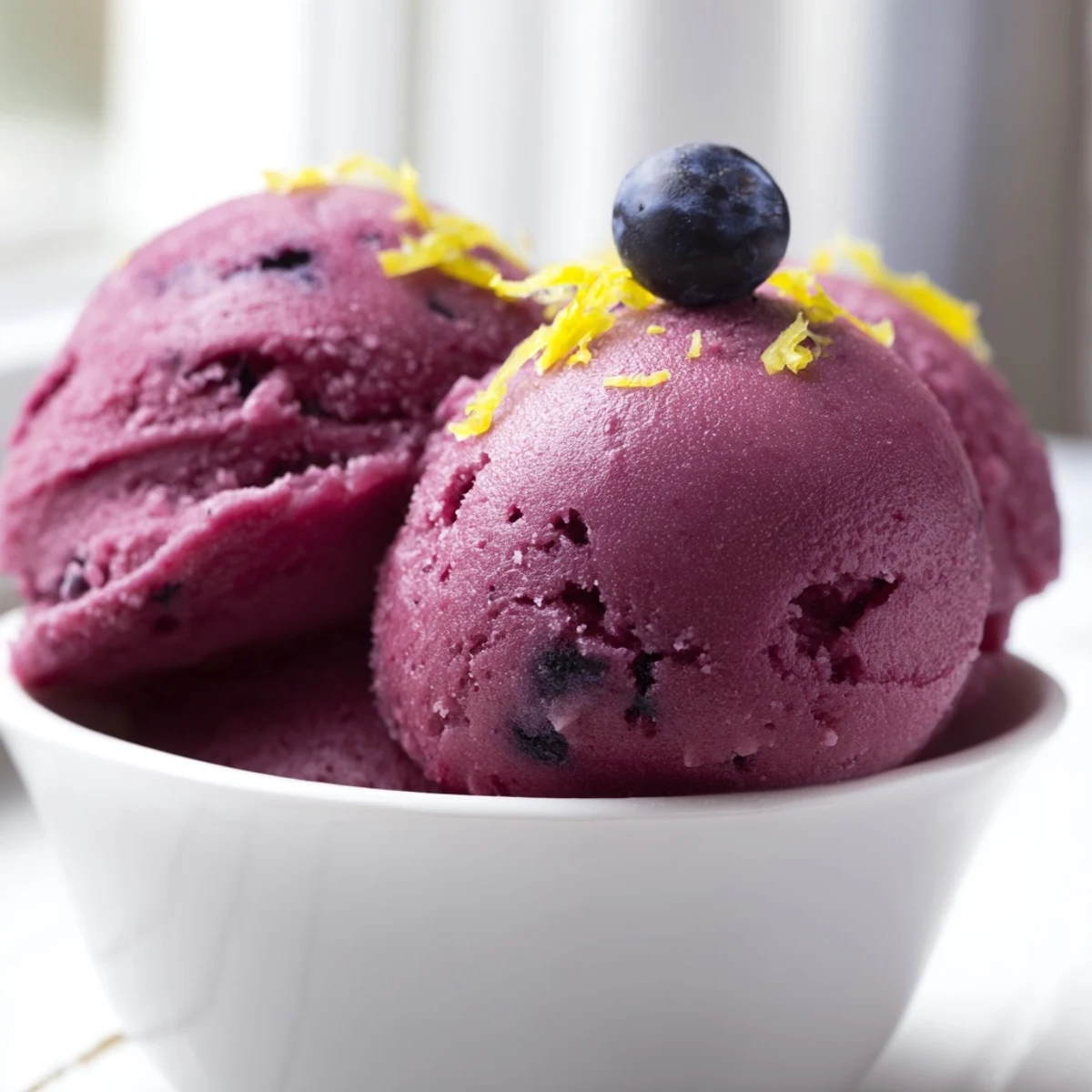 Creamy homemade blueberry lemon sorbet mounded in a white dessert bowl with lemon wedge
