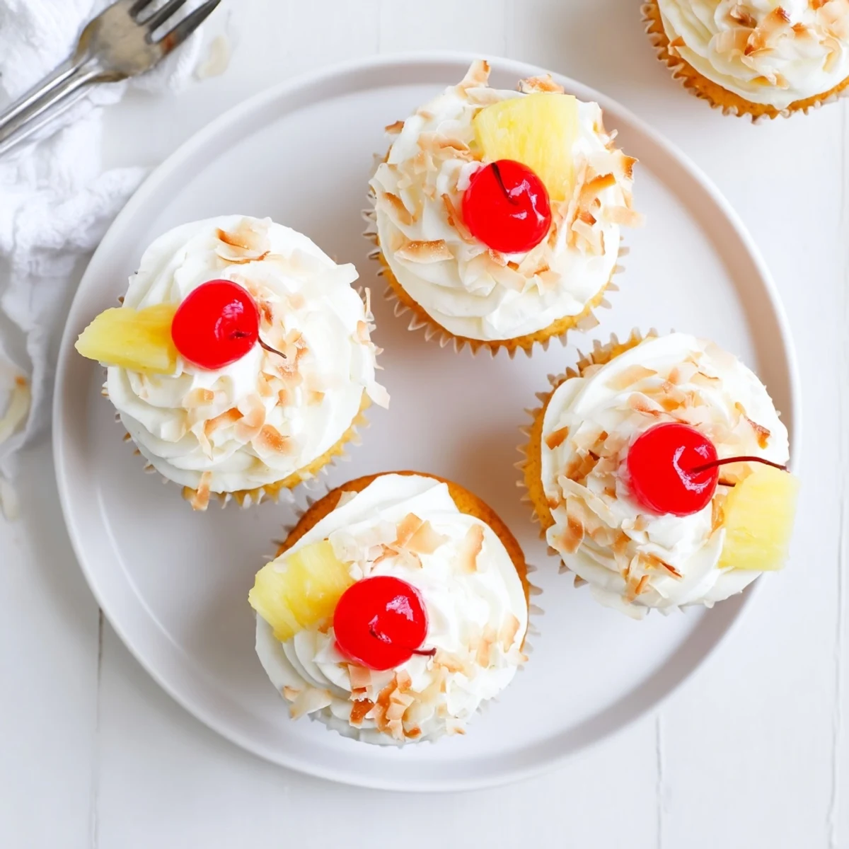 Pina Colada Cupcakes topped with fluffy white coconut frosting and garnished with toasted coconut flakes and red maraschino cherry
