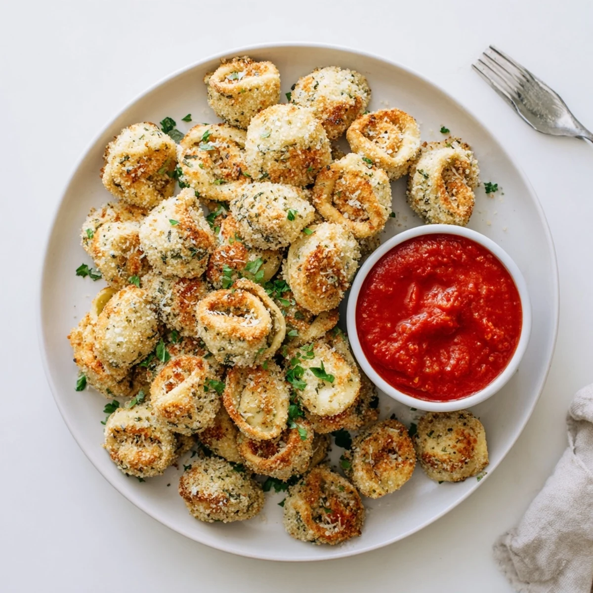 Golden air fryer tortellini arranged on a white platter with marinara dipping sauce