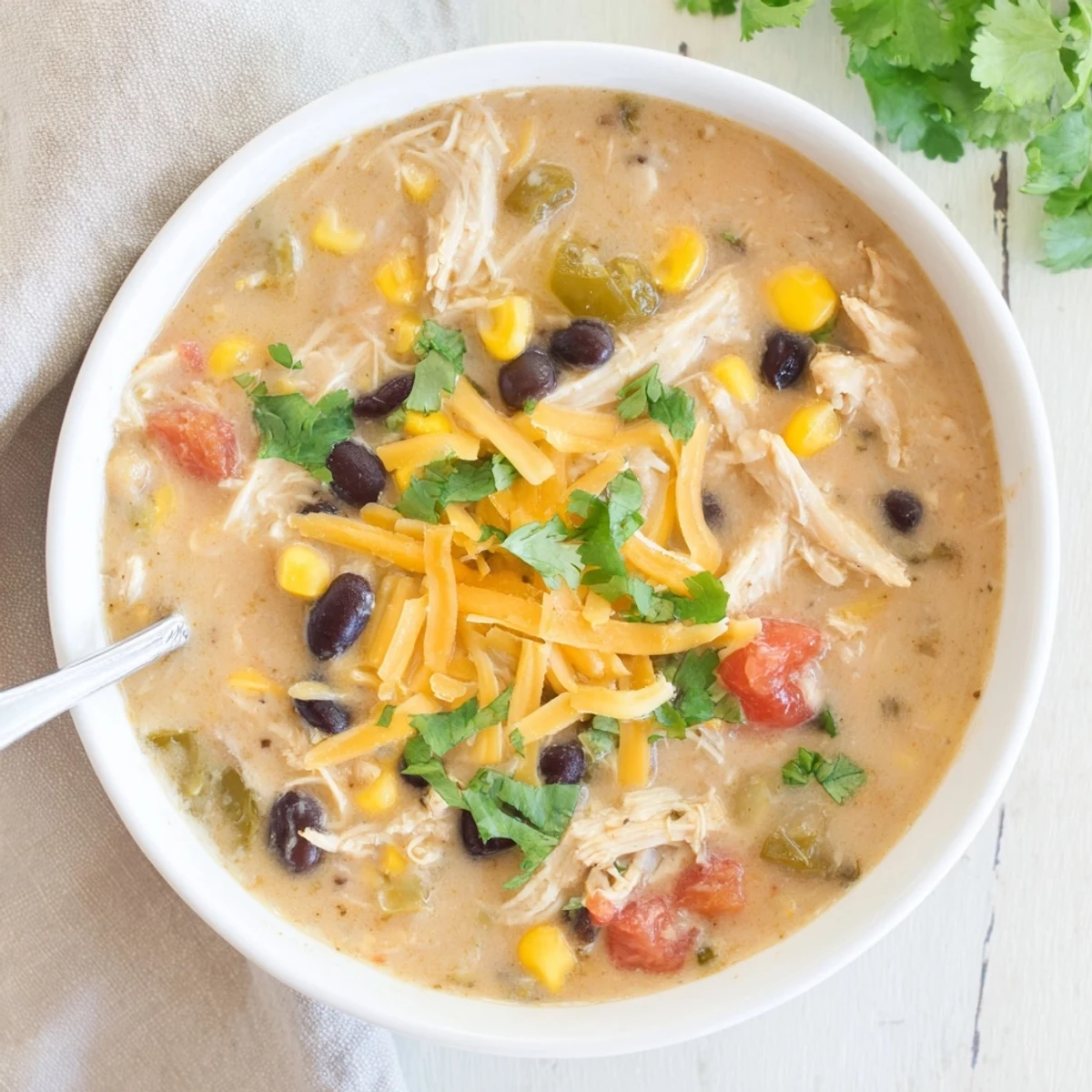 Bowl of easy creamy chicken taco soup garnished with cilantro, cheese, and crushed tortilla chips