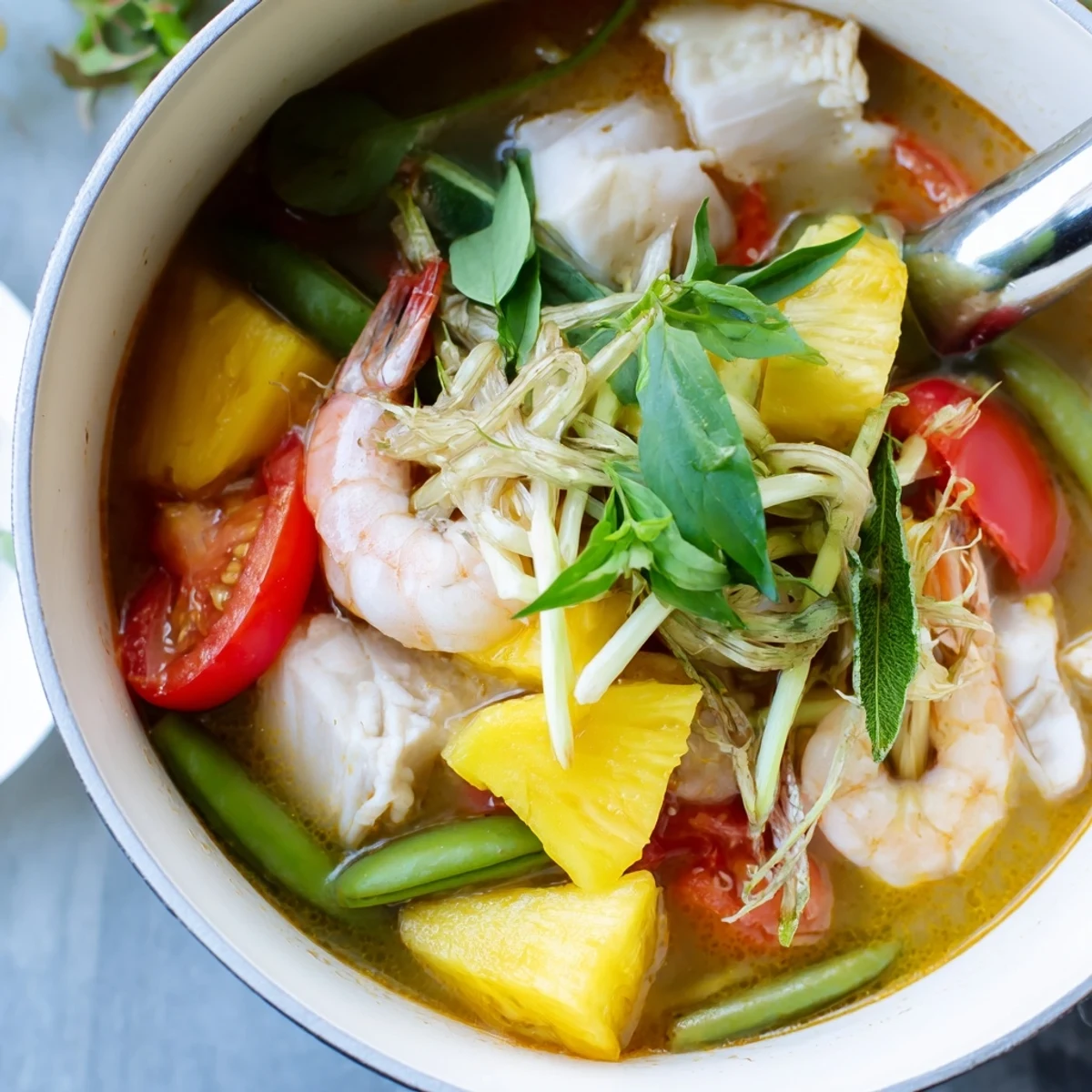 Golden bowl of tangy Canh Chua Vietnamese sour soup with pineapple chunks, fresh okra, and floating green onions