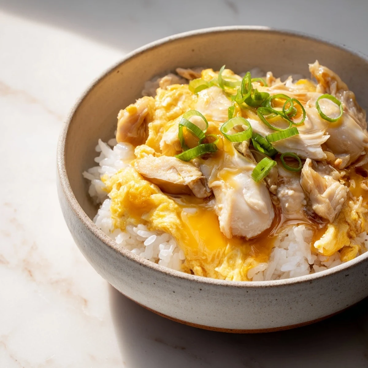 Golden Oyakodon bowl topped with fluffy scrambled eggs, tender chicken pieces, and sliced green onions over steaming white rice