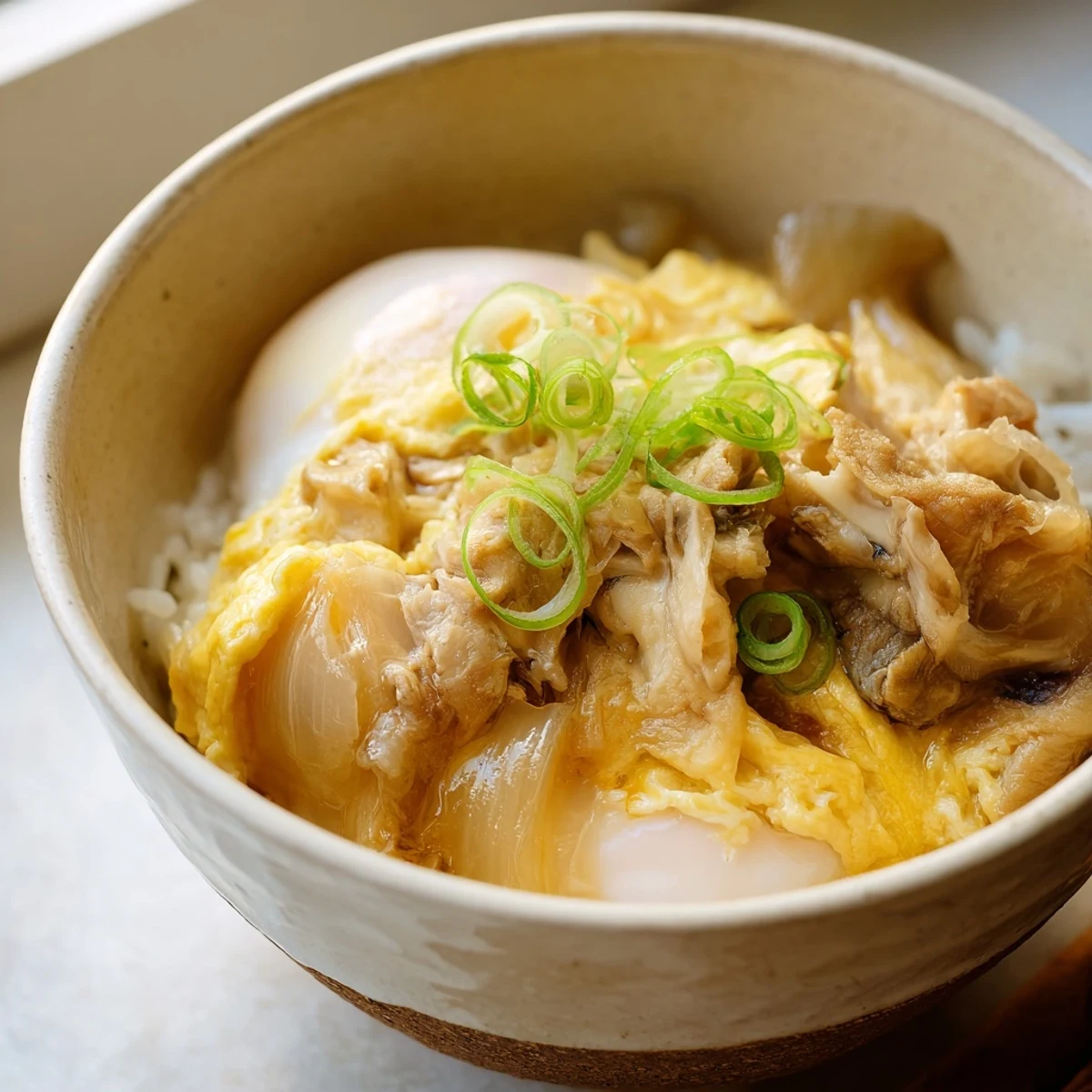 Homemade Japanese Oyakodon with juicy chicken thigh, caramelized onions, and silky egg sauce draped over a bed of fluffy rice