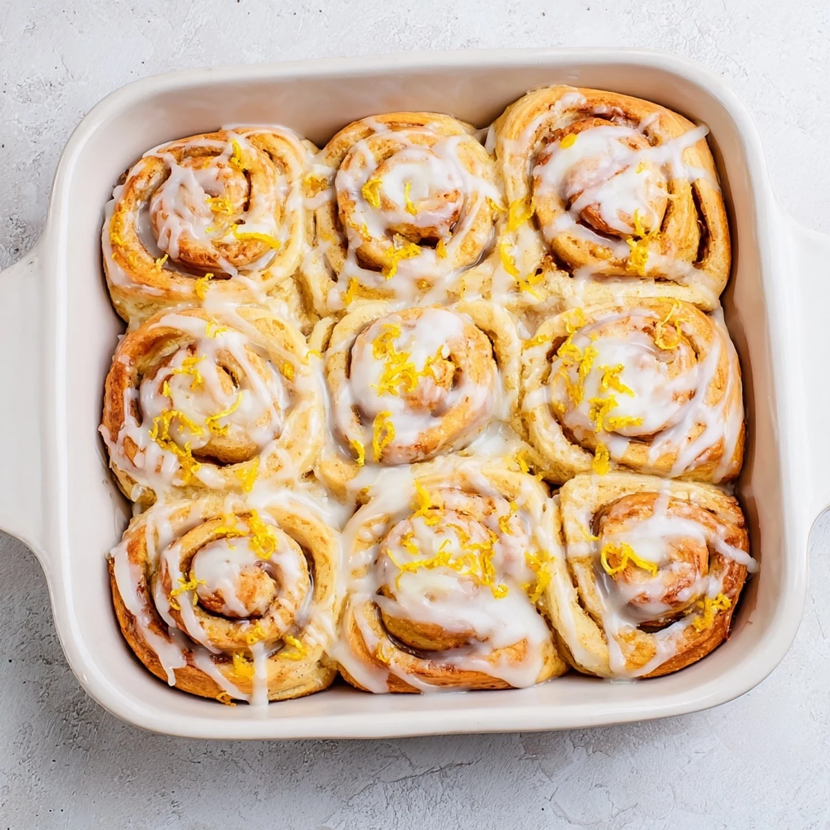 Fluffy homemade lemon rolls topped with white icing and fresh lemon zest