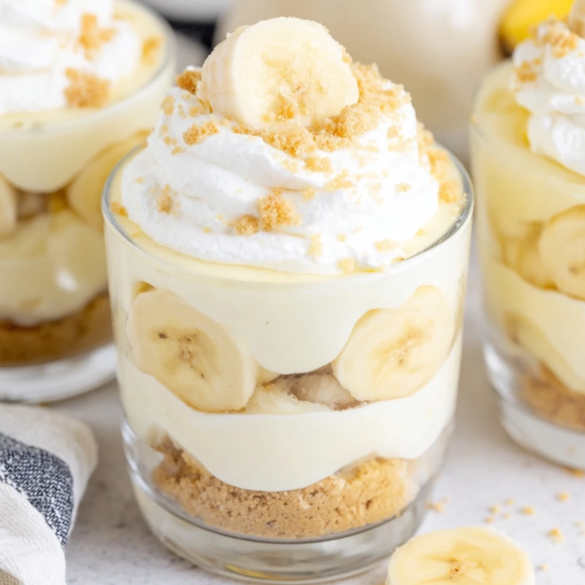 Creamy no bake banana pudding cheesecake cups topped with fresh banana slices and crunchy vanilla wafer crumbs