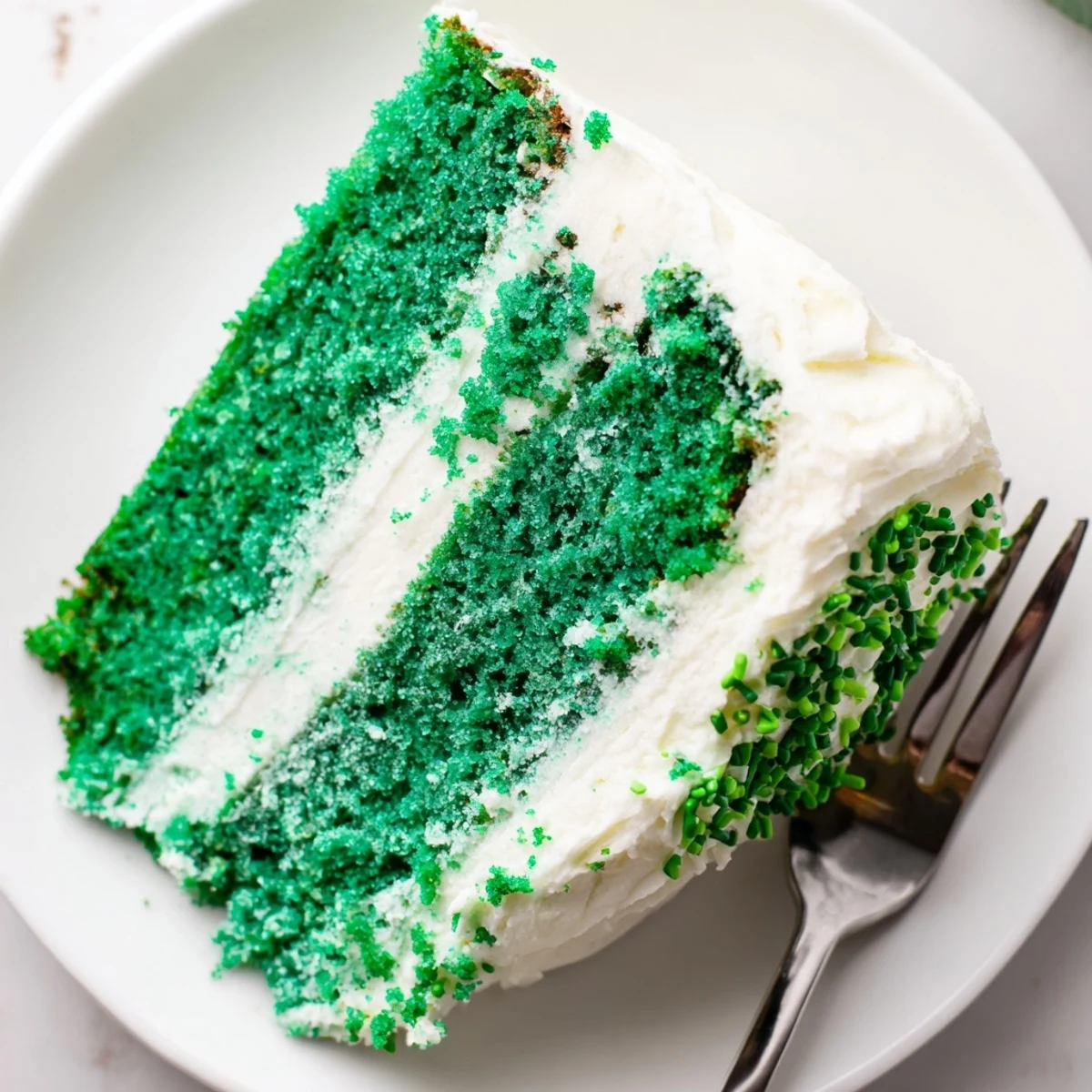 Moist green velvet cake layered with smooth tangy cream cheese frosting on white plate