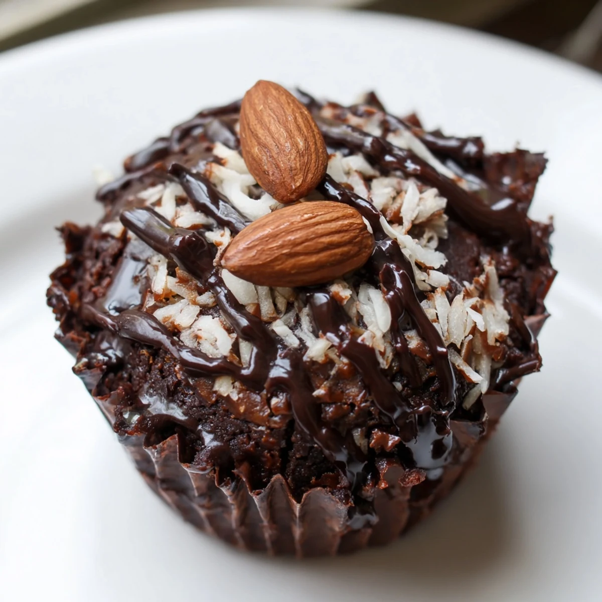 Rich Flourless Almond Joy Cupcakes topped with chocolate drizzle and roasted almonds on a rustic plate