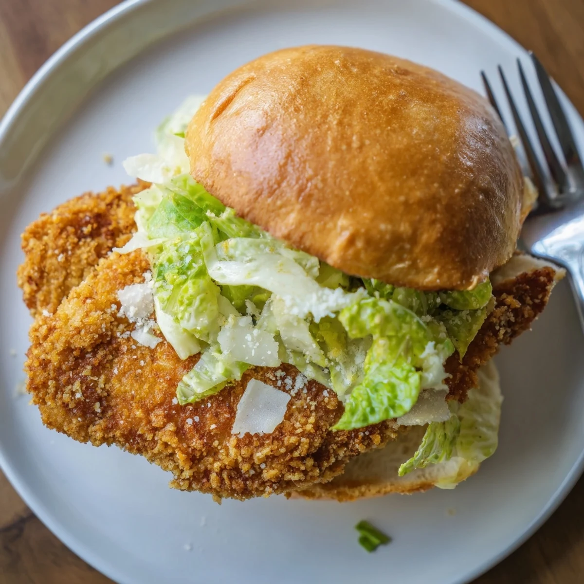 A sliced Crispy Chicken Caesar Sandwich Recipe with creamy dressing dripping, Parmesan shavings