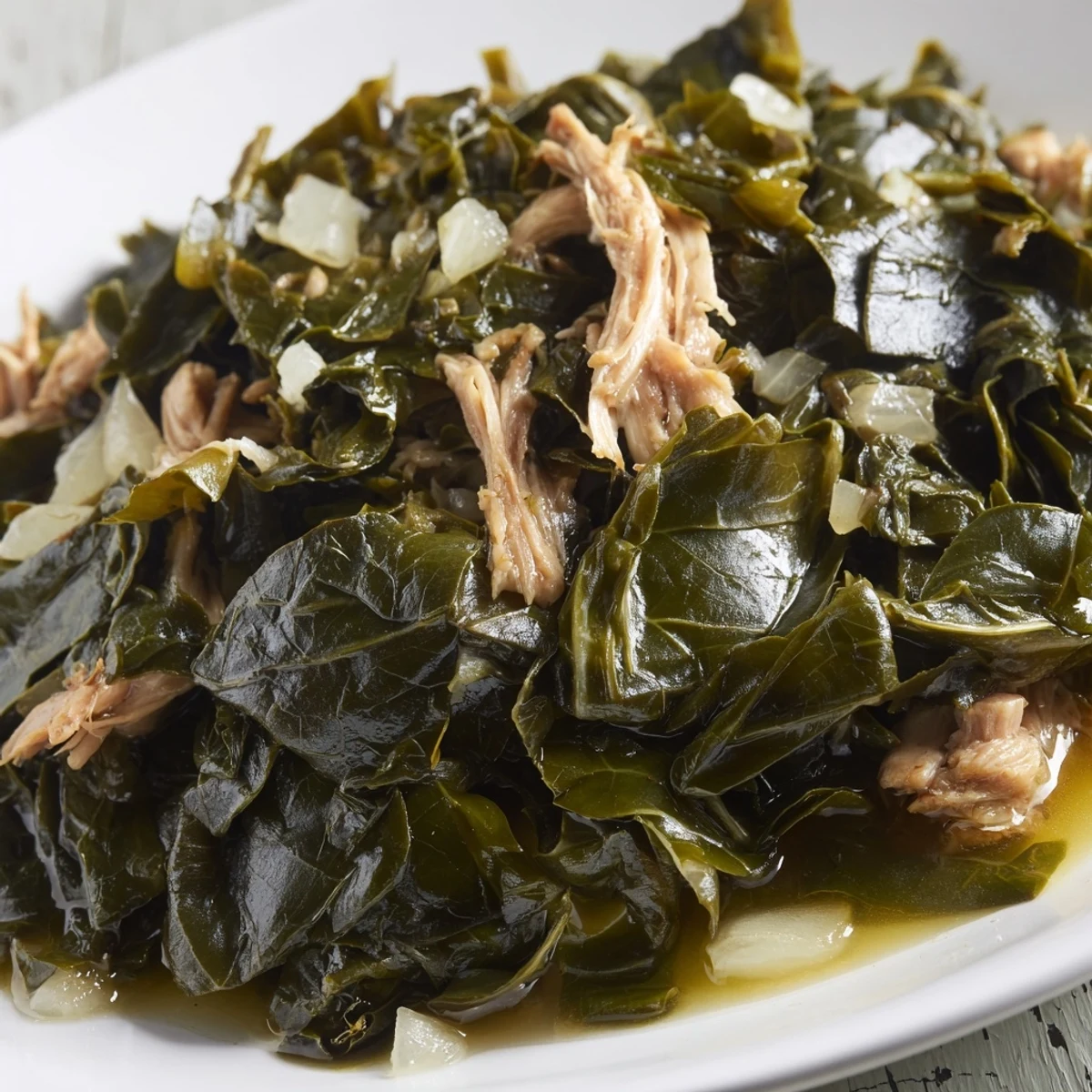 Hearty Southern collard greens with vibrant wilted leaves and savory broth, garnished with fresh black pepper on a wooden table