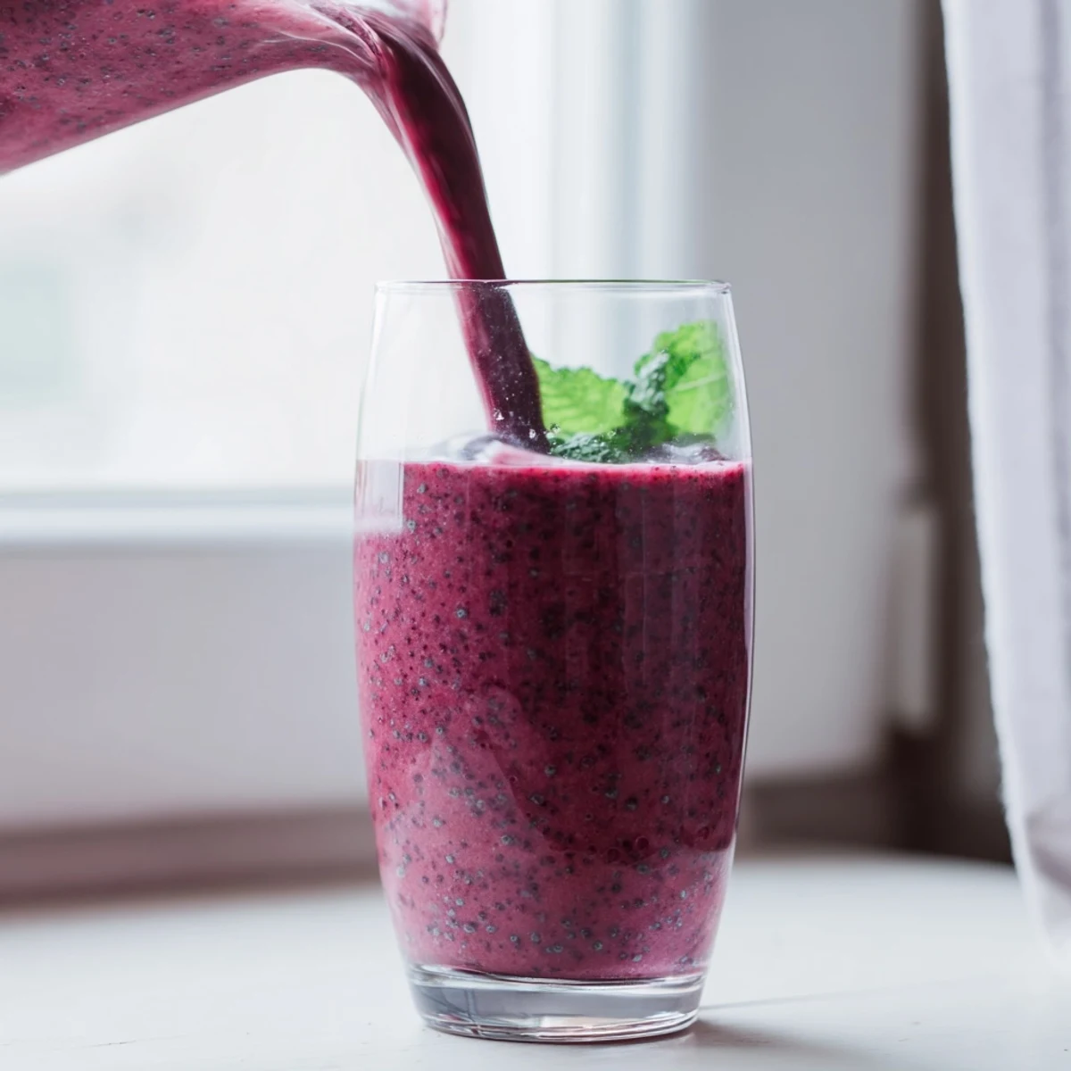 Thick purple beet smoothie blended with strawberries and banana, topped with chia seeds and mint sprig