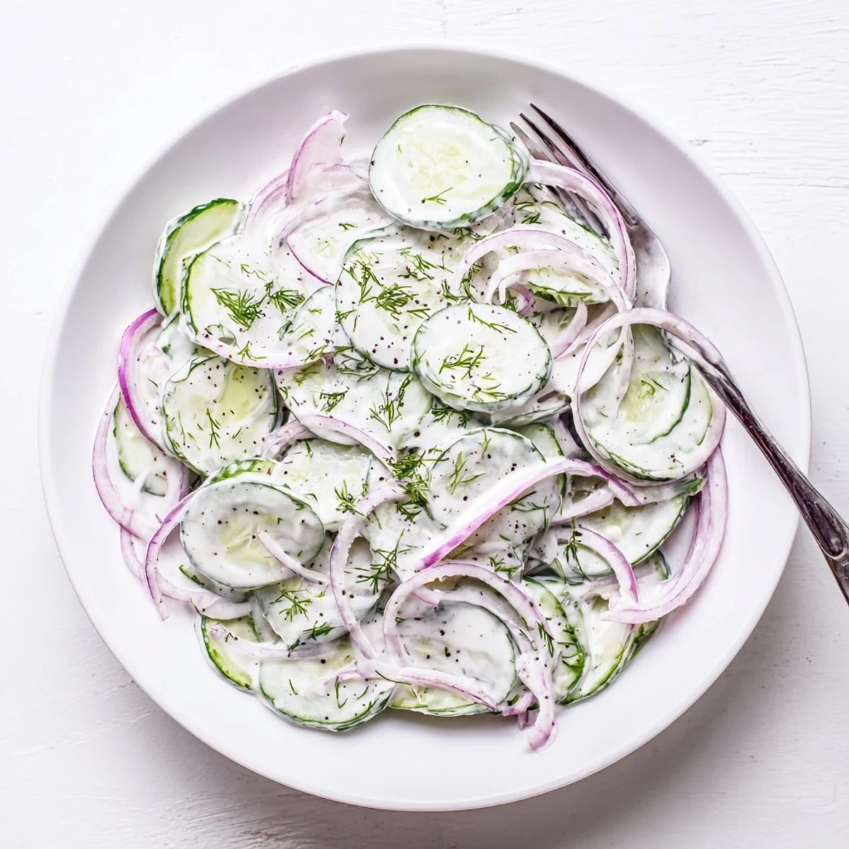 Crisp cucumber dill salad topped with chopped fresh herbs in a white serving bowl