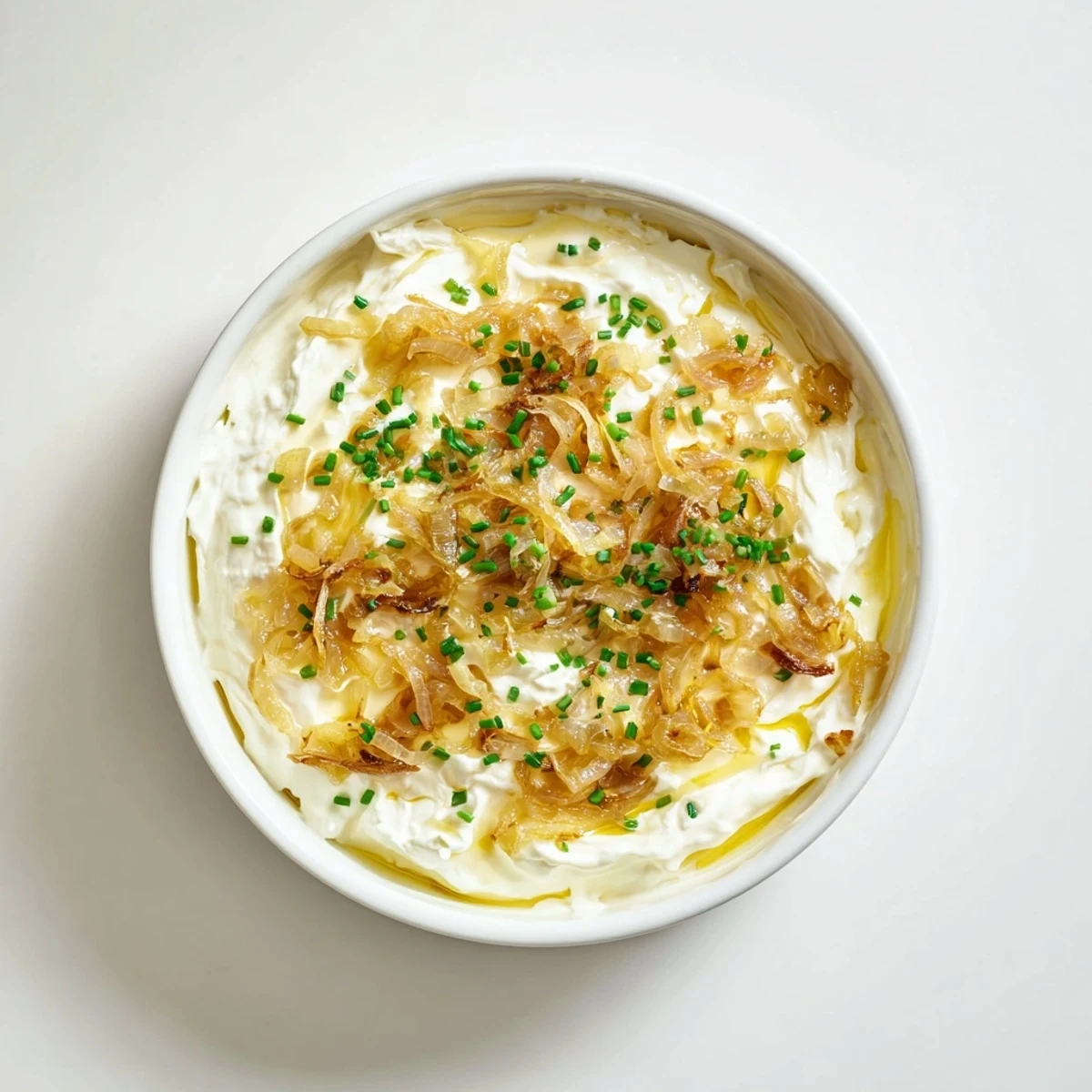 Creamy French onion dip topped with caramelized onions and fresh chives beside crispy potato chips