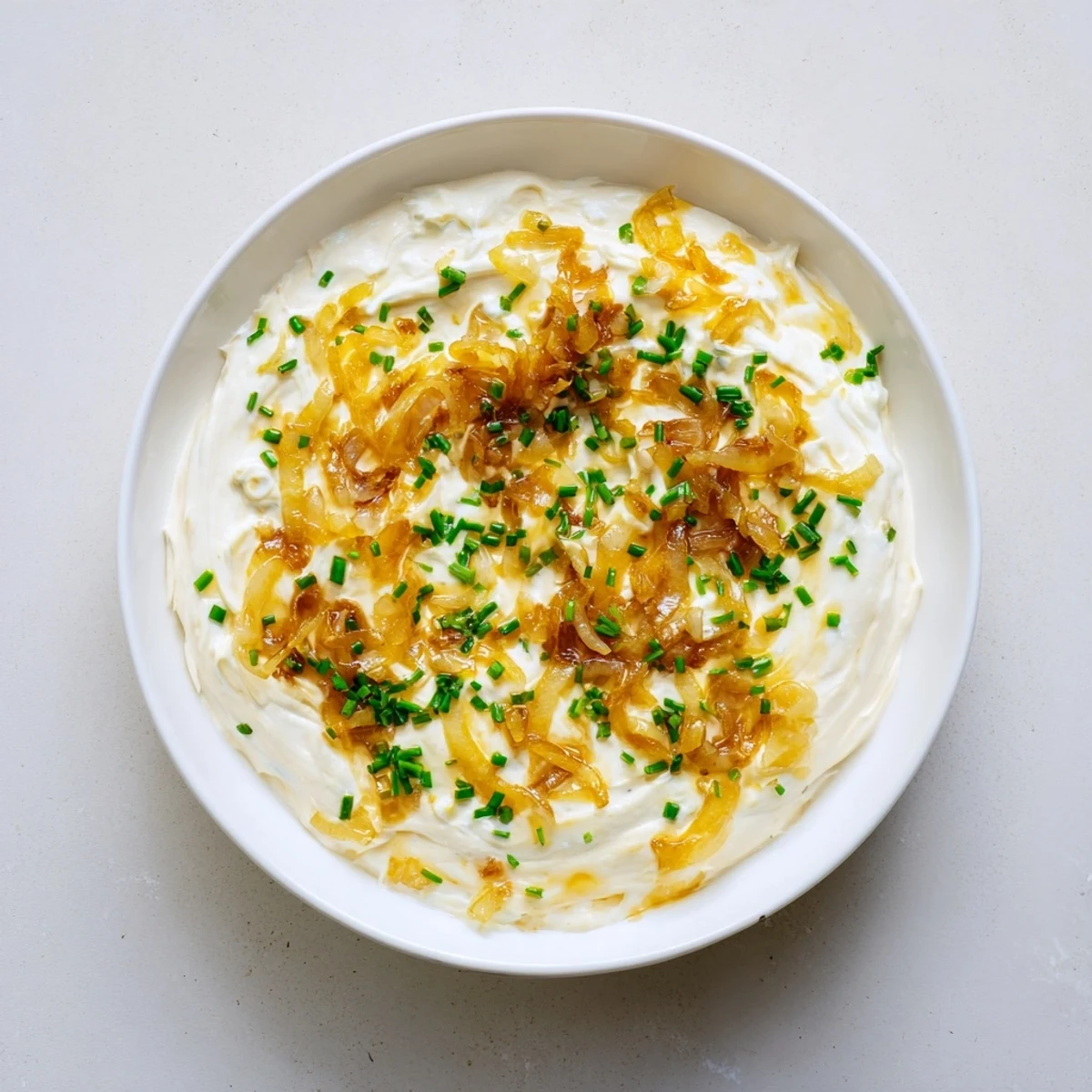 Rich French onion dip in a white bowl garnished with green onions served with tortilla chips