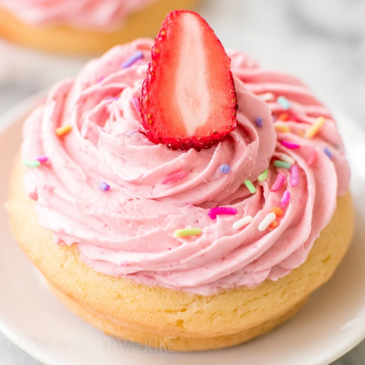 A dozen homemade strawberry buttercream frosted donuts arranged on a wire cooling rack