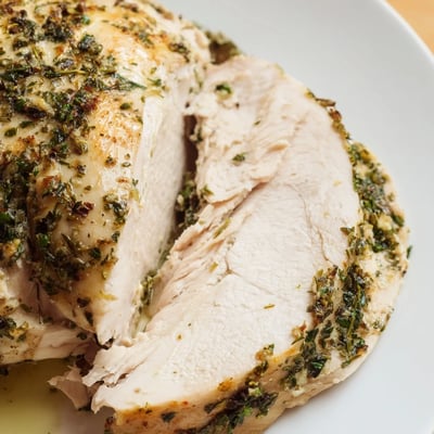 Sliced Savory Herb Roasted Turkey Breast revealing juicy, tender meat served alongside roasted vegetables and a drizzle of pan jus.