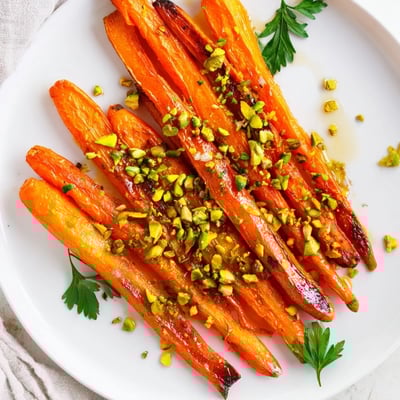 Roasted carrots with honey and pistachios served warm, garnished with fresh parsley on a rustic platter.